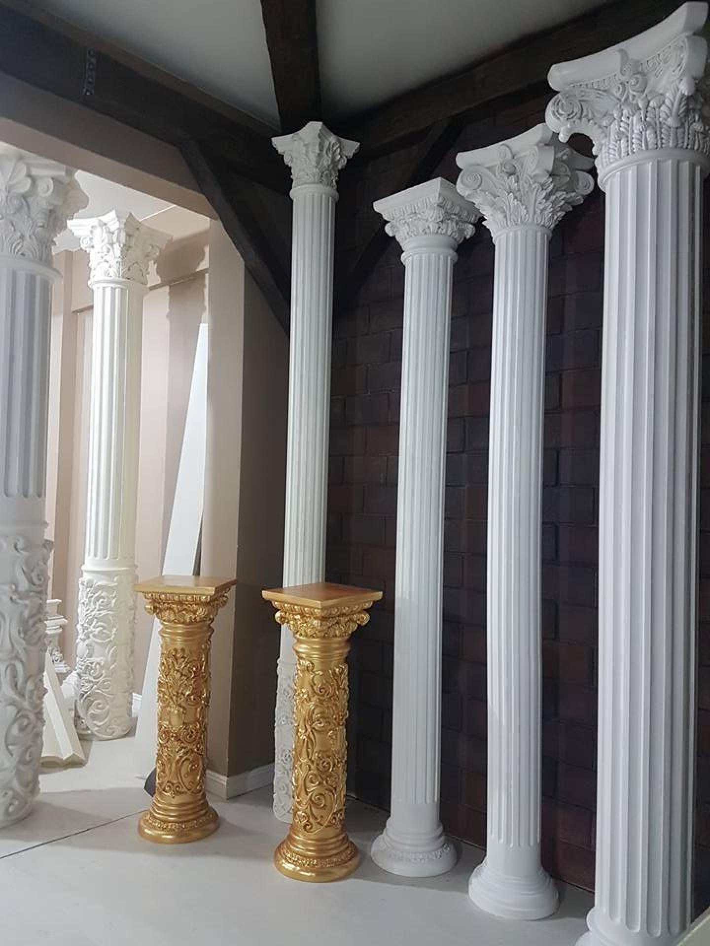 Eleganti colonne scanalate in poliuretano bianco con capitelli corinzi e basi in foglia d'oro su sfondo di mattoni scuri.