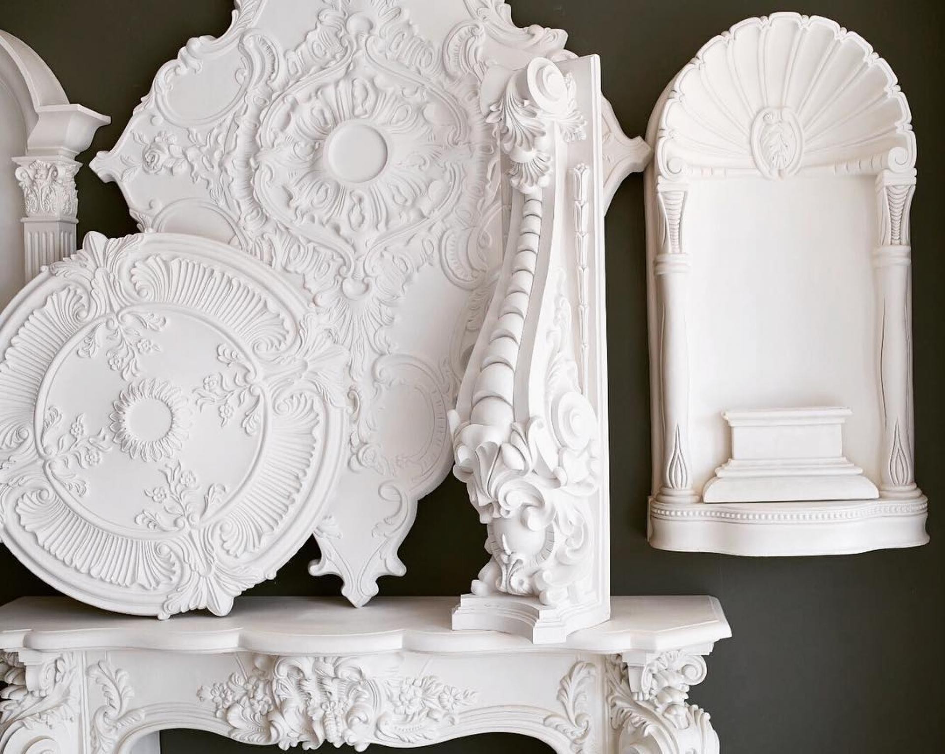 Rosoni in poliuretano bianco, nicchie e mensole decorative esposte su sfondo scuro per design d'interni classico.