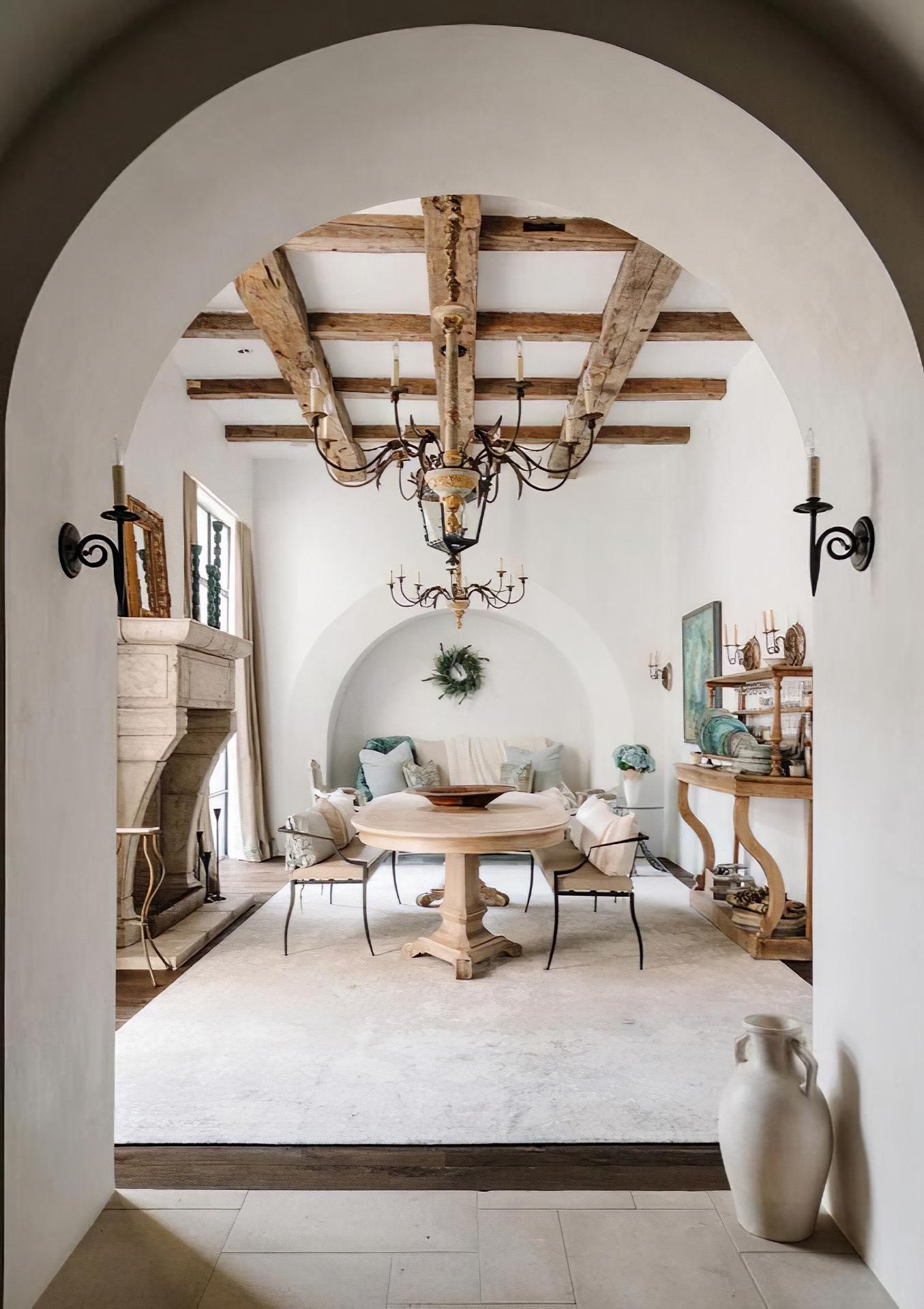 Sala da pranzo neoclassica con travi in poliuretano Polure effetto legno, camino in pietra e archi architettonici.