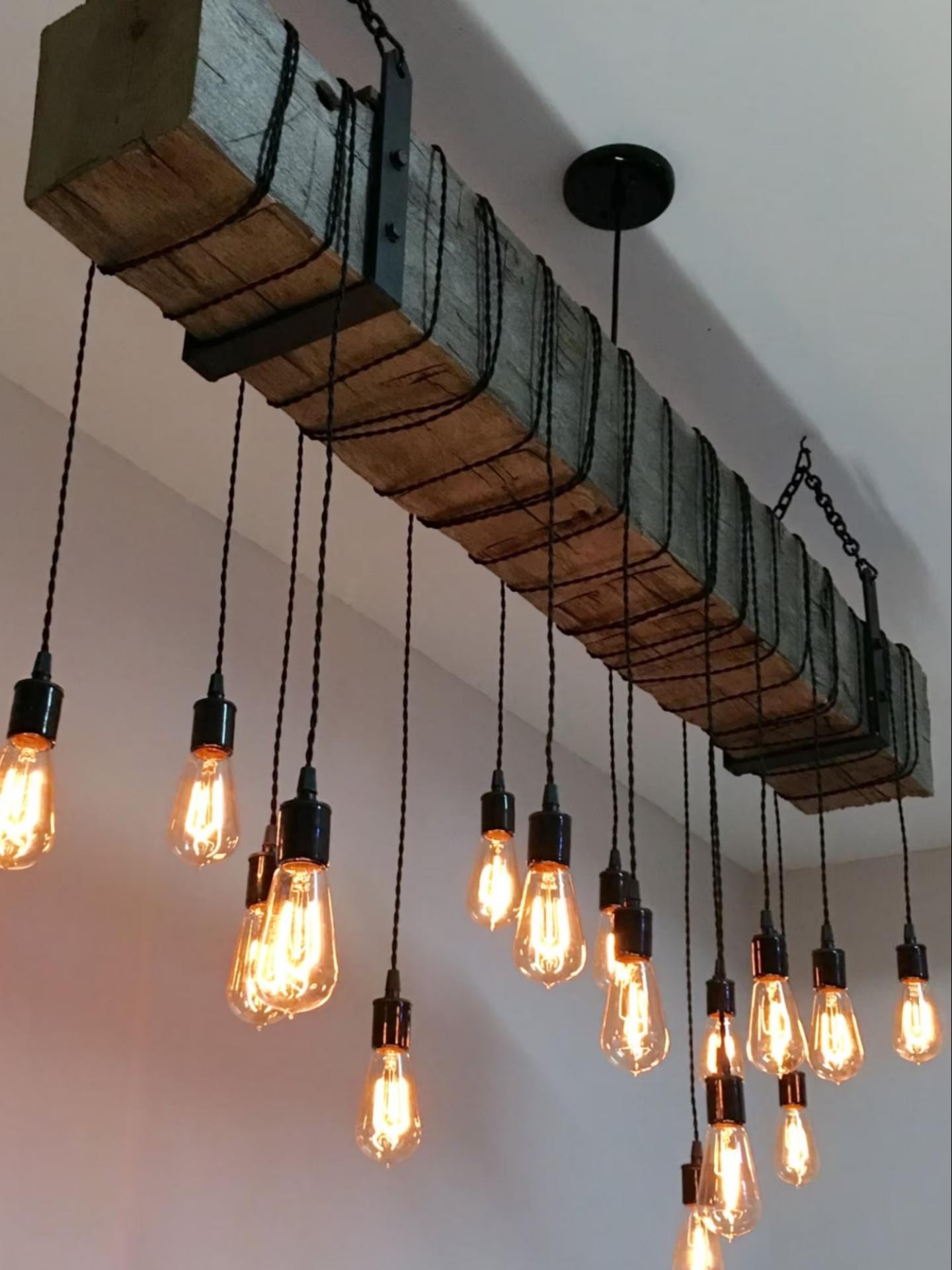 Trave decorativa in poliuretano effetto legno con lampadine Edison sospese su sfondo di parete grigia moderna.