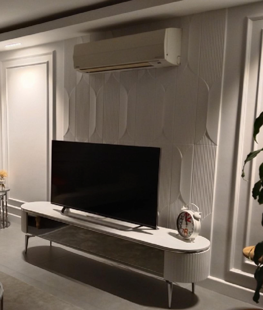 Modern bir salonda TV ünitesi arkasında beyaz geometrik dokulu poliüretan duvar paneli ve yanlarda düz duvar çıtalama uygulaması.