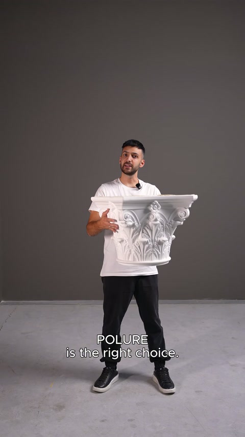 Il presentatore mostra un capitello di colonna bianco lavorato con ampi motivi acantei