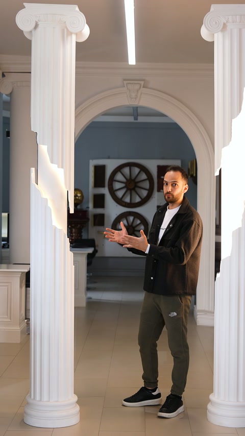 Presenter stands between two fluted columns in arched interior space