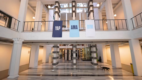Üniversite atriyumunda merdivenler, galeriler ve sergi alanı görülüyor