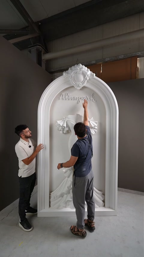 Two craftsmen examine lettering placement above the central bridal-dress sculpture.