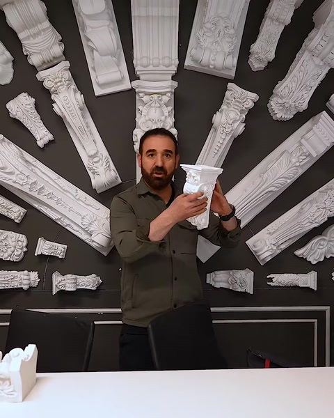 Uomo che tiene un pezzo di capitello compatto accanto a un muro di esposizione di colonne