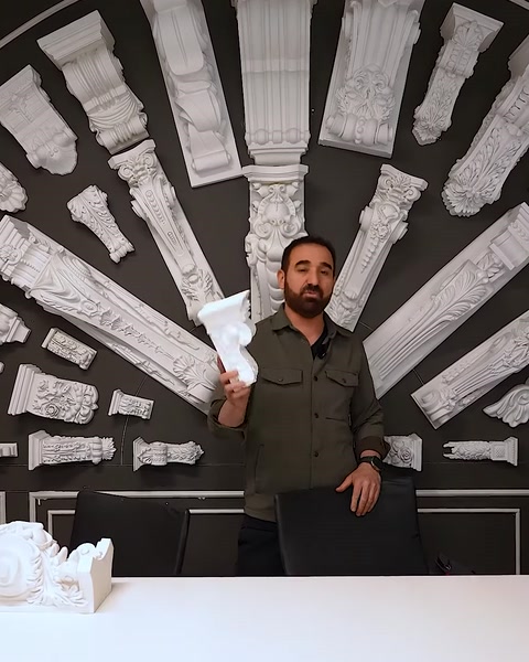 Uomo che tiene un piccolo capitello davanti a un muro di esposizione completo di capitelli