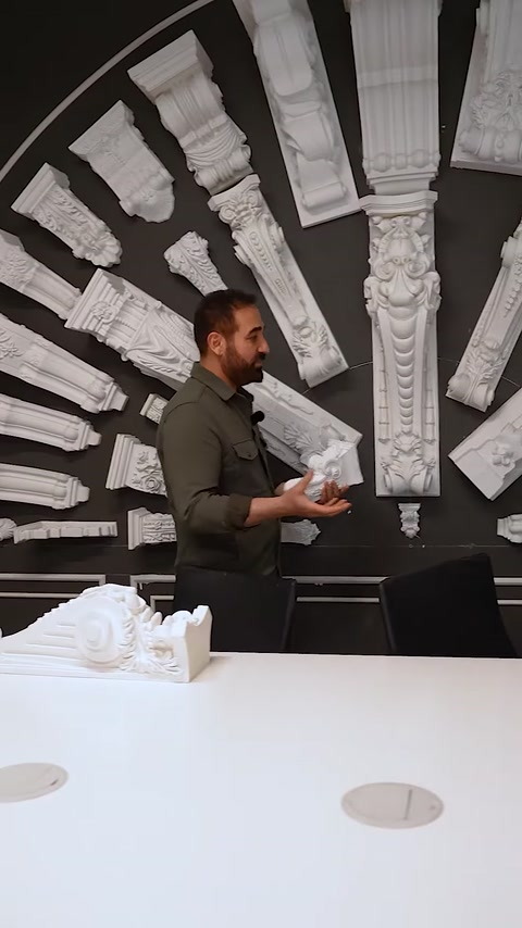 Uomo che tiene un piccolo capitello davanti a un muro di esposizione di grandi capitelli