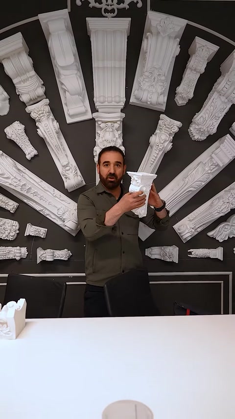 Uomo che tiene un pezzo di capitello compatto accanto a un muro di esposizione di colonne