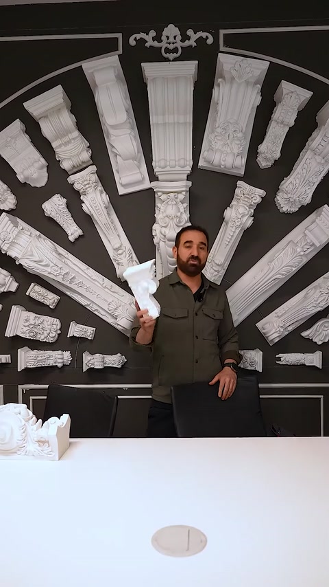 Uomo che tiene un piccolo capitello davanti a un muro di esposizione completo di capitelli