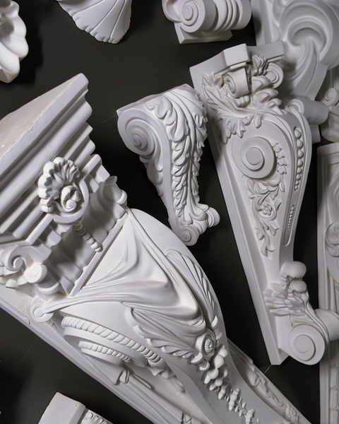 Mensole e corbelli decorativi intagliati montati su una parete scura del salone espositivo