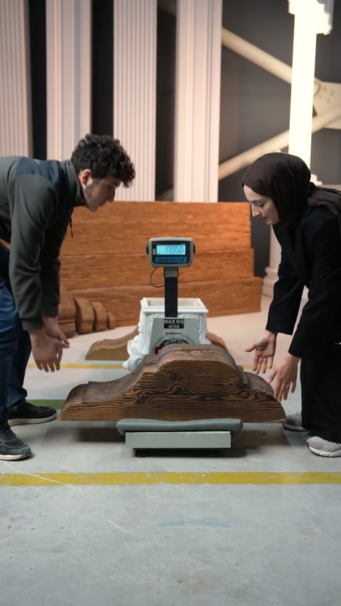 Due operai posizionano una grande cornice in legno sulla bilancia digitale.