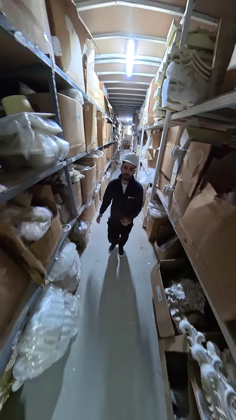 Employee walks distant warehouse aisle filled with stacked product boxes