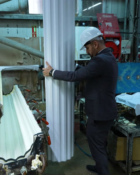 Worker holds white polyurethane column profile near machine
