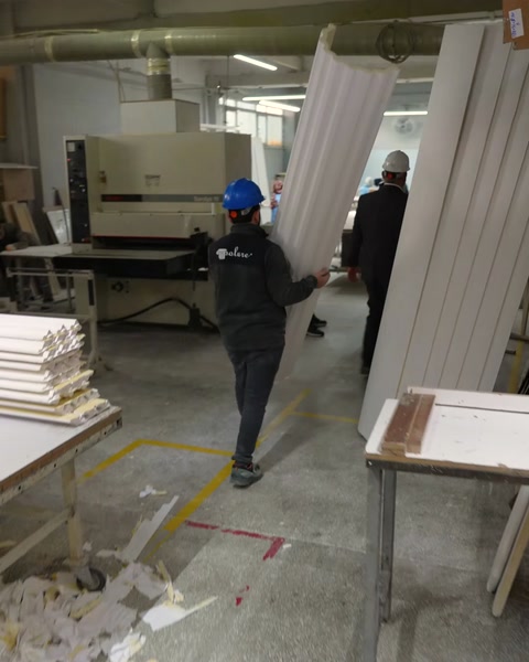Worker carries finished white polyurethane cornice profiles in workshop