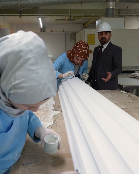 Workers hand-finish white polyurethane cornice profile surface detail