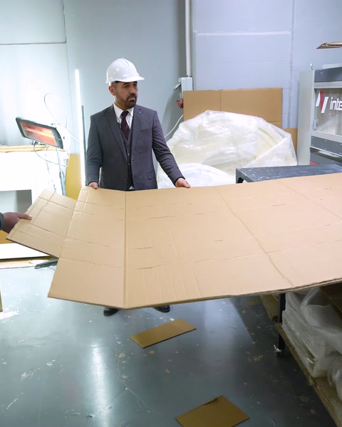 Manager carries large cardboard packaging sheet in workshop