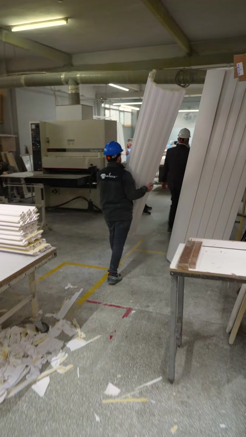 Worker carries finished white polyurethane cornice profiles in workshop
