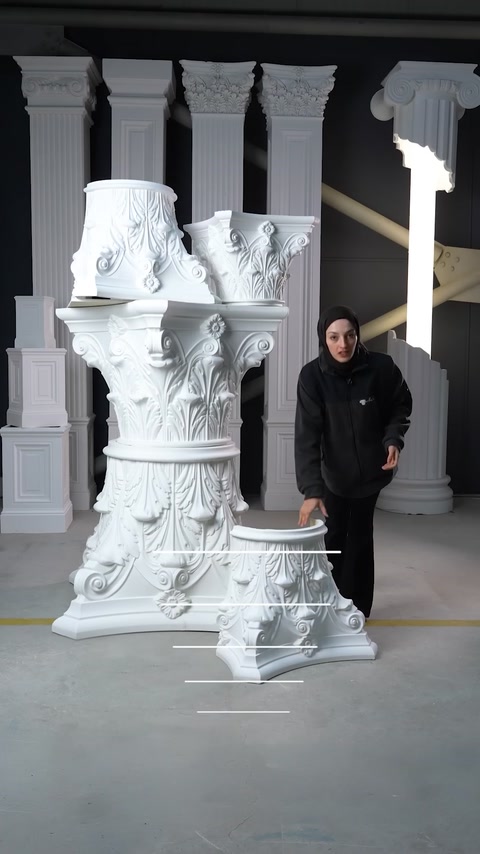 Capitelli per colonne ornati di diverse dimensioni sono disposti accanto alle colonne dello showroom.