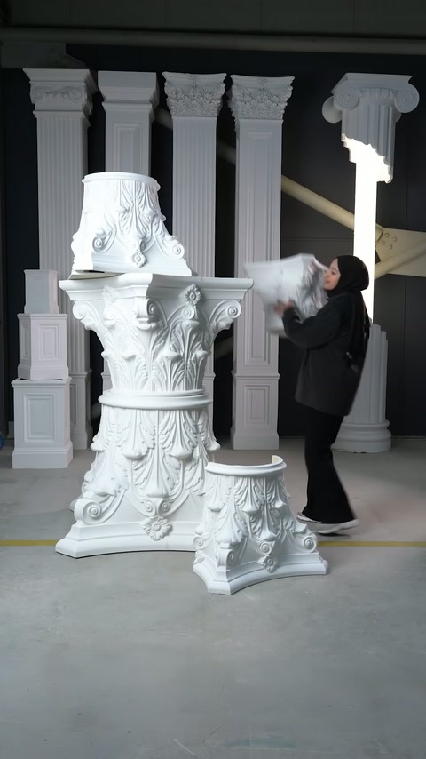 Il presentatore solleva un capitello ornamentale più piccolo accanto ai pezzi di assemblaggio esposti.