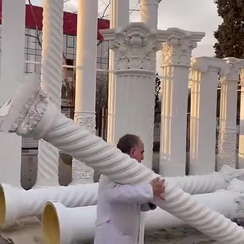 Un artigiano trasporta con entrambe le mani un lungo elemento di colonna tortile