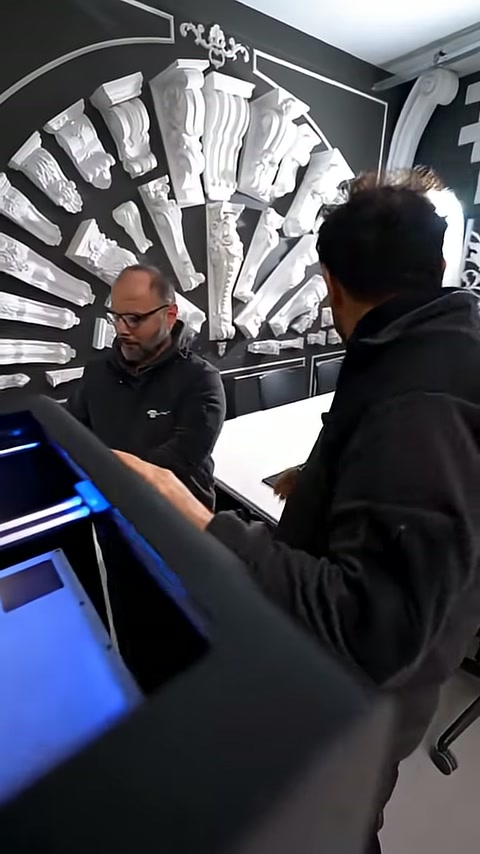 Staff members at the machine evaluate the small produced piece.