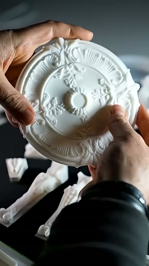 The embossed features of a circular ceiling rose held in hands are examined.