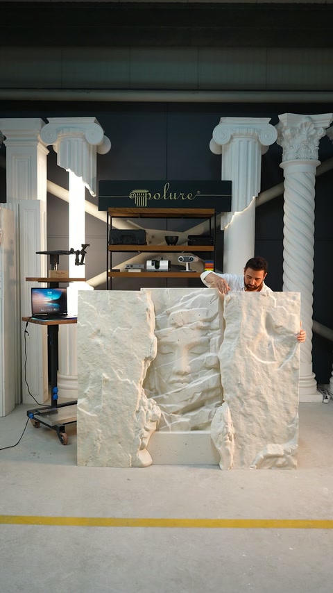 Man aligns three freestanding relief panel sections across the workshop floor.
