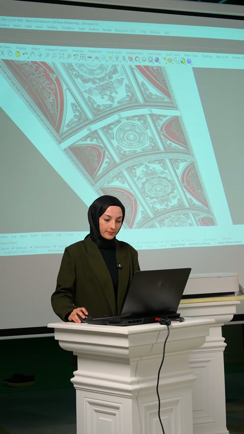 Il conduttore prosegue la presentazione utilizzando il computer davanti al design del soffitto curvo