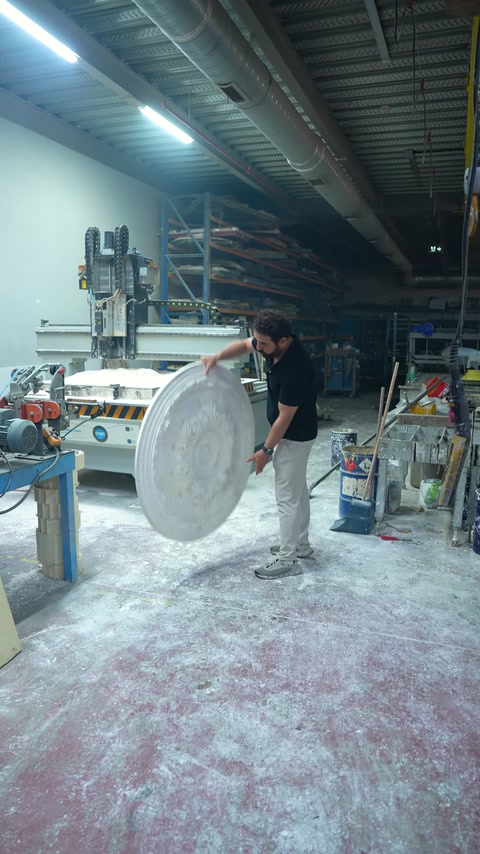 A large circular ceiling medallion is being carried beside the production bench.