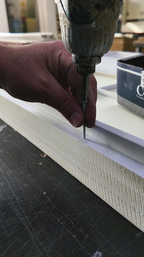 A worker fastens a slim profile strip during panel assembly