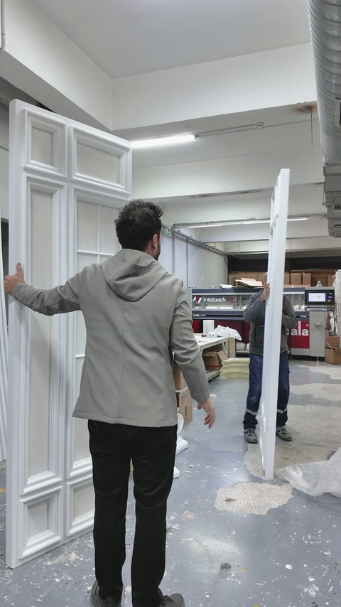 Workers compare upright panel sections while arranging the mirrored composition