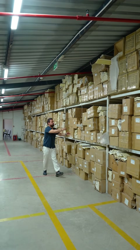 Designer moves through wide warehouse among boxed stock and decorative profiles.