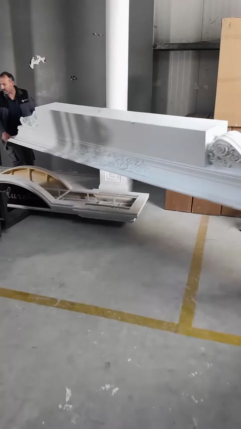 Un lungo elemento decorato della corona superiore viene trasportato da due addetti.
