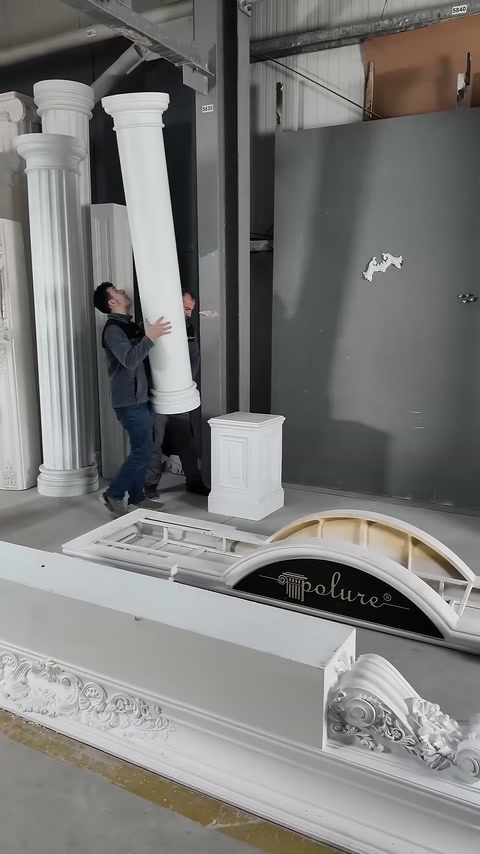 Two workers carry the white column body together in upright position.