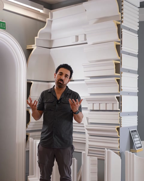 Man presenting stacked polyurethane cornice moulding profiles in showroom.
