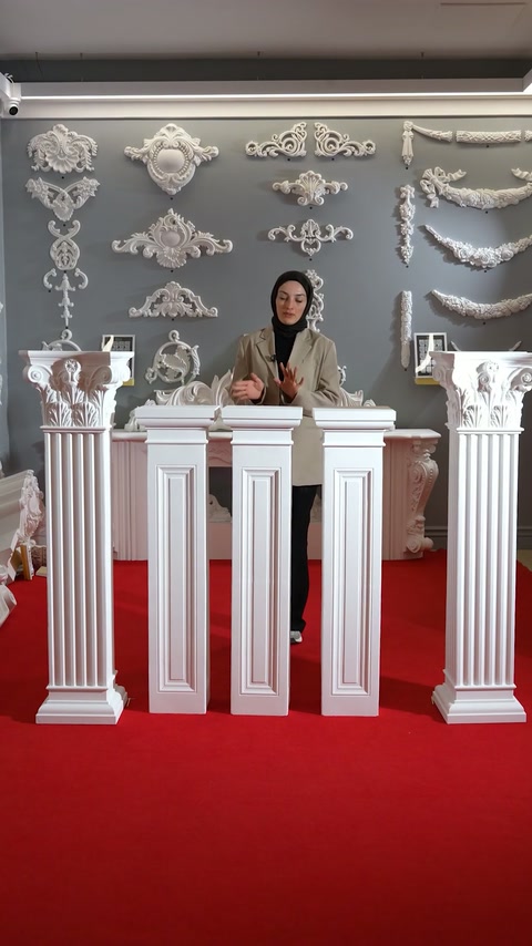The presenter stands behind square and fluted decorative pedestal models.