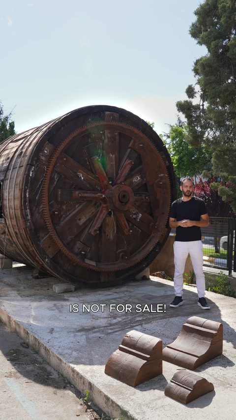 A presenter explains decorative pieces beside a large wooden wheel