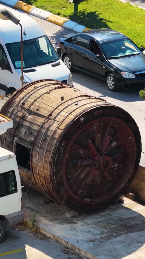 A barrel-shaped wooden object is seen from above beside a parking area