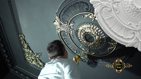 A craftsman paints the decorations around the ceiling medallion with a brush