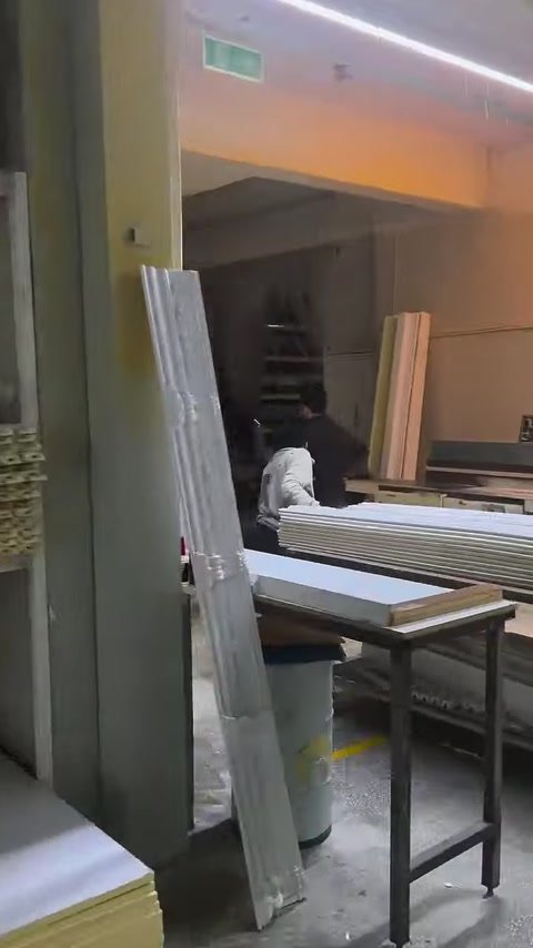 A craftsman prepares long white decorative profiles on a machine workbench.
