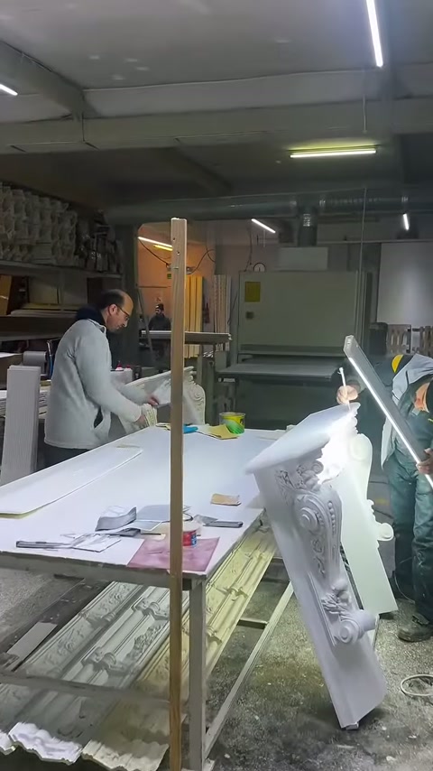 A craftsman examines a white column capital by hand at the work table.