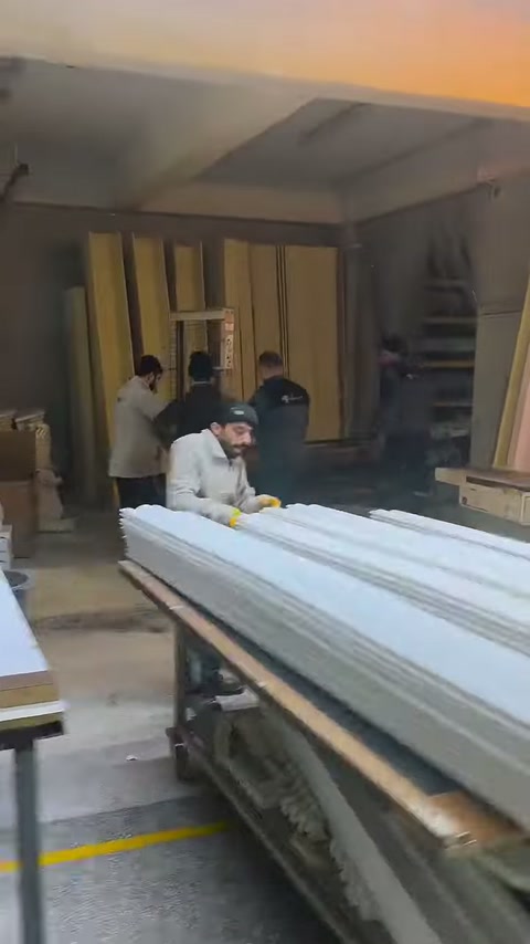 Workers arrange long white profiles across a wide production table.