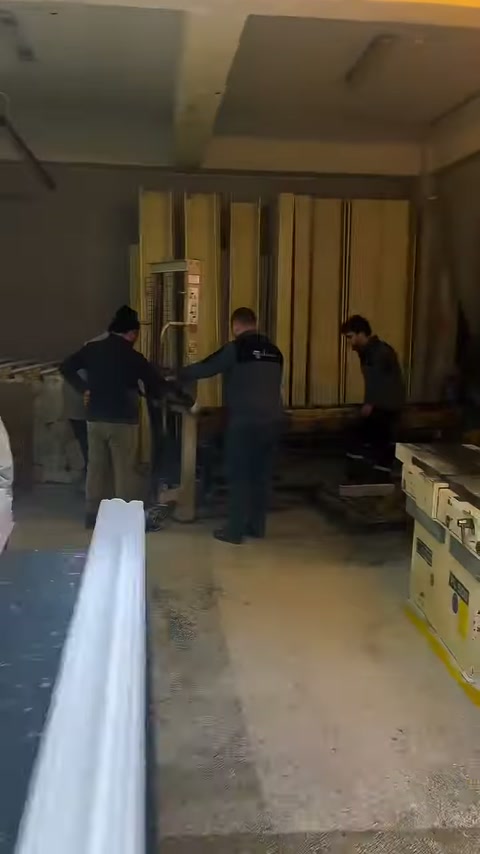 Three workers prepare around long decorative parts.