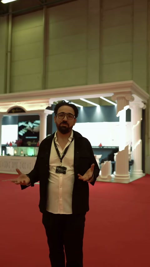 Il presentatore illustra il progetto decorativo della facciata davanti a uno stand fieristico con colonne.