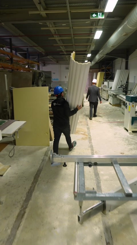 Two workers carry a large decorative profile inside the factory