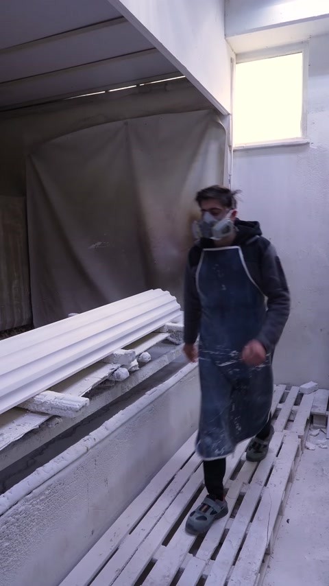 A worker wearing protective equipment spray-paints white profiles