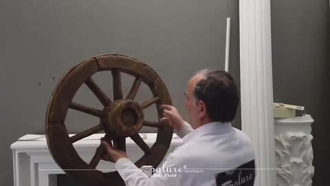 Il presentatore esamina una ruota decorativa da carro di colore scuro sulla parete