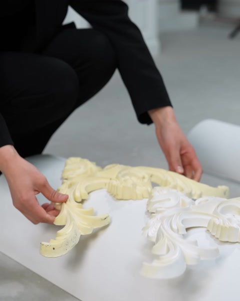 Mani che dispongono pezzi di modanatura color crema e bianca su una superficie curva