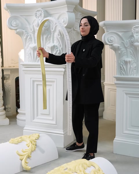 Donna in piedi che tiene una modanatura flessibile color crema curva accanto a colonne